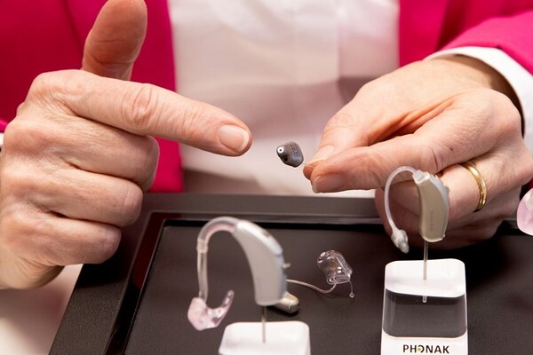 Eine Person zeigt verschiedene moderne Hörgeräte und erklärt deren Funktionen.